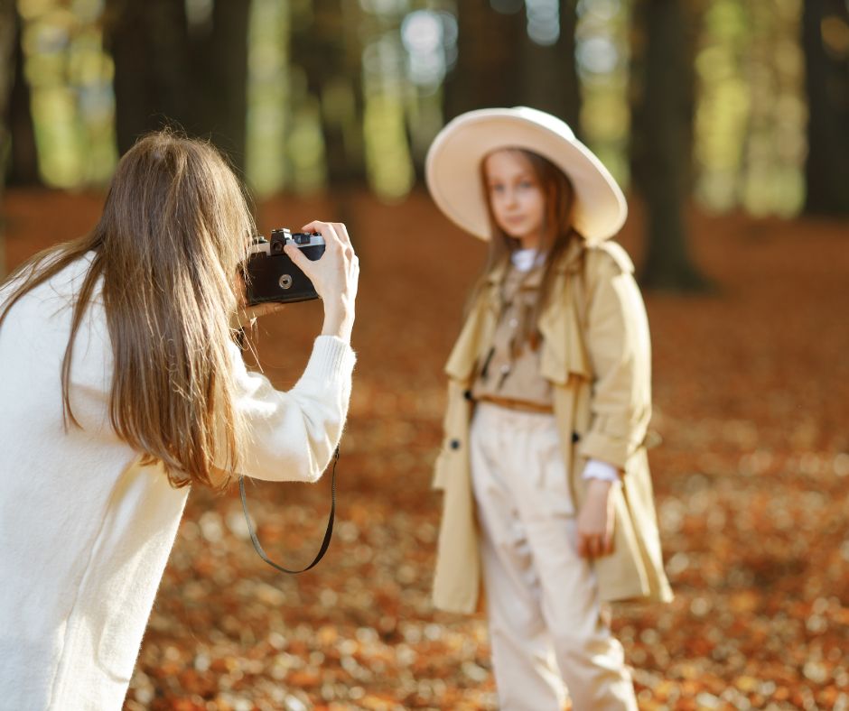 Mother takes photos of daughter in fall foliage.