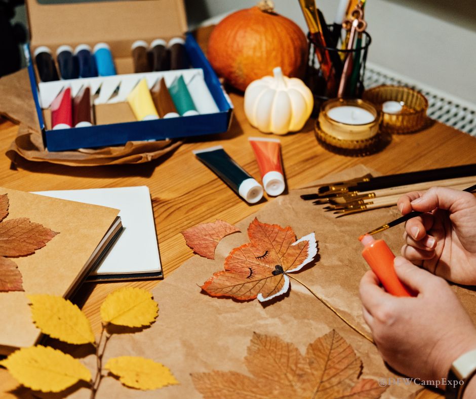 A pair of hands is doing simple fall crafts at home, the table is covered in fall leaves and a brown paper bag.