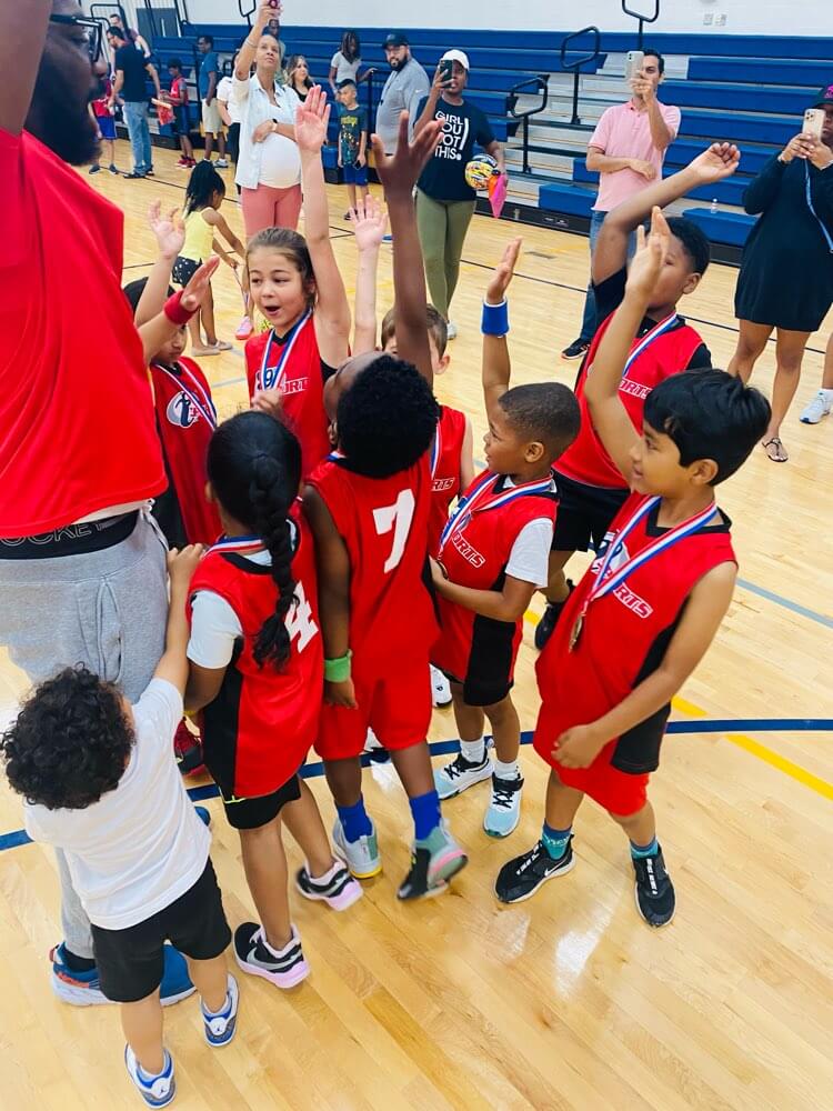 Children in red basketball uniforms joining a team huddle after a game