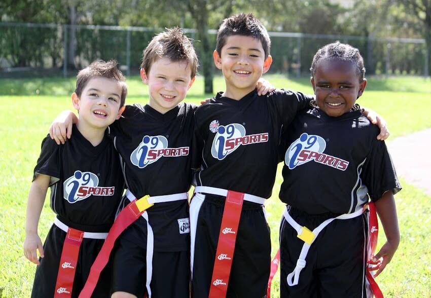 Four young flag football teammates standing together in i9 Sports uniforms