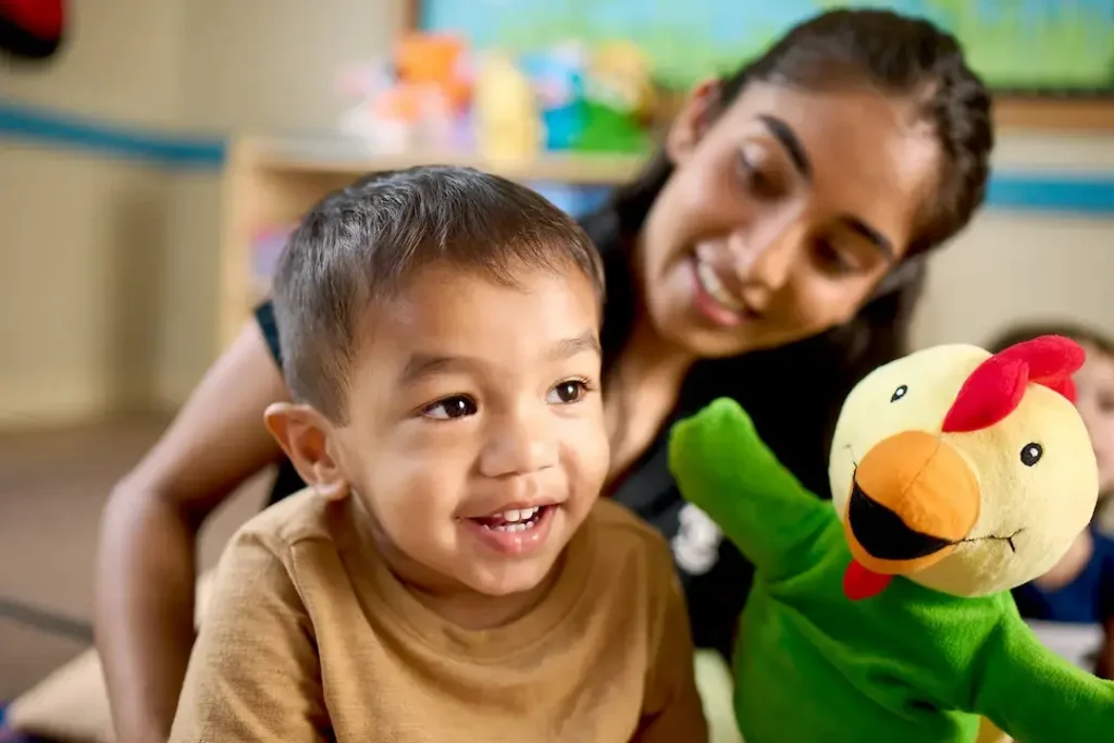 Preschool teacher engaging a young child with a colorful puppet during playtime